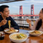 Sepasang kekasih sedang menikmati Mie Celor Palembang dengan kuah udang gurih yang kental, disajikan bersama udang segar, telur rebus, tauge, dan taburan bawang goreng, menjadi salah satu kuliner legendaris khas Sumatera Selatan yang menggugah selera. (Foto: Adit/Sriwijayaterkini.co)